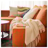 Orange couch, beige blanket, colorful pillows, side table