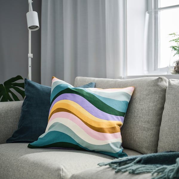 Brightly colored wave-pattern throw pillow on grey sofa, near window.