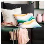 Brightly colored cushion with wavy stripes on a black couch. Accompanied by a light pink blanket and vases.