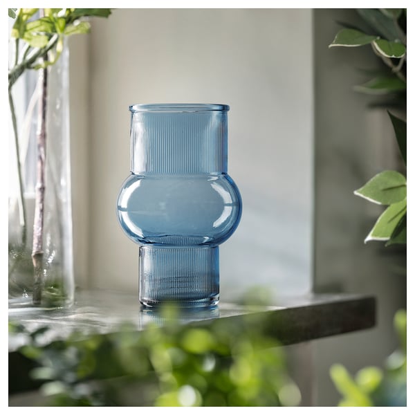 Blue recycled glass vase, ribbed design, unique shape, on shelf with plants.