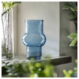 Blue recycled glass vase, ribbed design, unique shape, on shelf with plants.