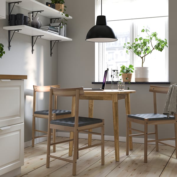 Cozy dining nook with NACKANÄS table, dark-cushioned chairs, and green plants.