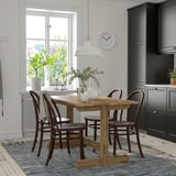 Cozy dining area with wooden table, chairs, pendant lamp, and decorative vase.