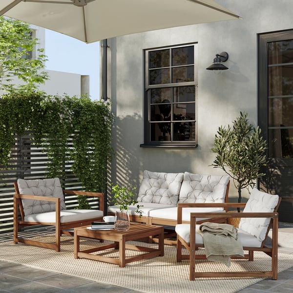 Modern outdoor patio with NÄMMARÖ wooden furniture set, including a sofa and two chairs with white cushions, under a beige umbrella.
