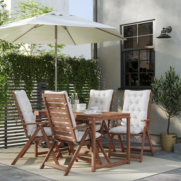 Modern patio set with wooden table, four folding chairs, white cushions, and a large beige umbrella.