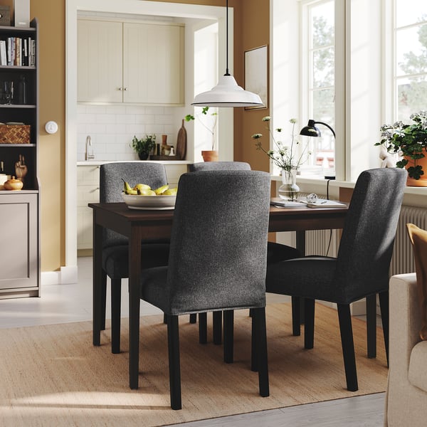 Dining room with dark chairs around wooden table, bowl of fruits. Kitchen with white cabinets, well-lit, cozy.