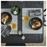 Dinner setup with two plates of fish, onion, and herbs; two glasses, silverware, and a seasoning dish on a dark wooden table.
