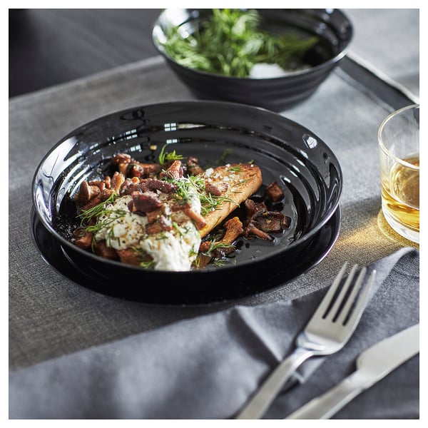 Black dish with bread and mushrooms. Glass plate on table, fork and knife beside it.