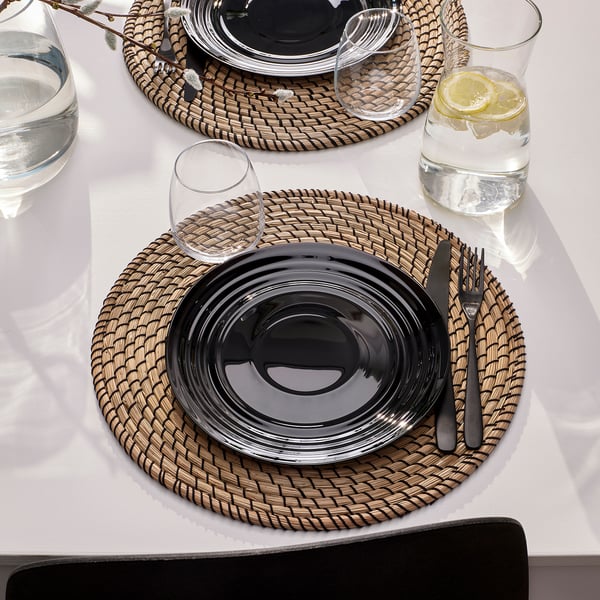 Table set with NÄTBARB glassware, featuring circular, glossy plates and matching glass cups with lemon slices on a white tablecloth, ready for dining.