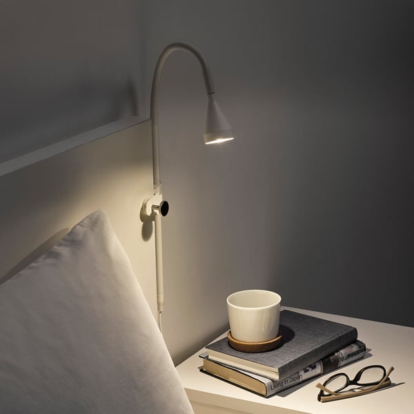 Wall-mounted adjustable light with warm glow on bed frame, beside cup and books.