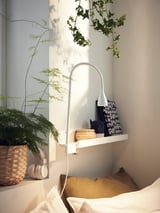 Bedside sleek white NÄVLINGE lamp, adjustable on shelf with books, headphones, plant.