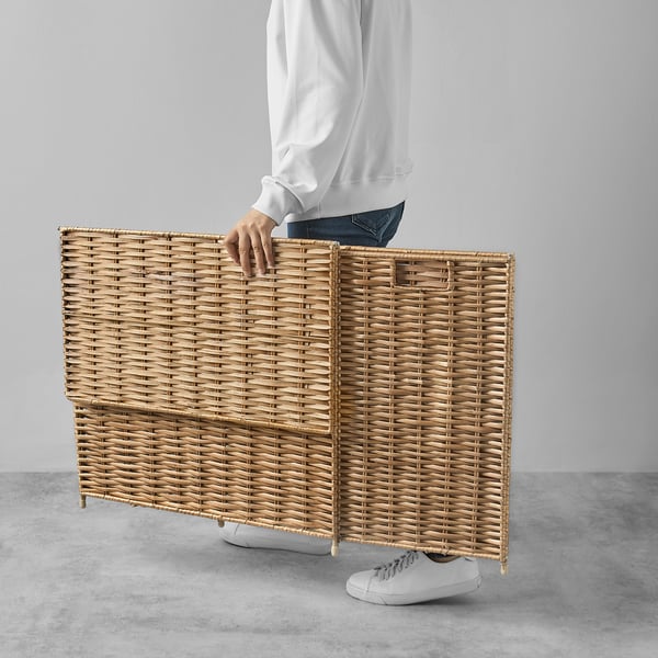 Person holding a lightweight, flat-packed willow laundry basket with two compartments for sorting clothes.