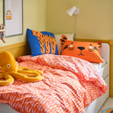 Cozy kids bed with orange tiger pillows. Bright, playful design. White bedside lamp, plush toy, and wall art complete the vibrant, inviting space.