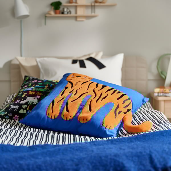 Bed with blue tiger cushion, striped blanket, and colorful pillow.