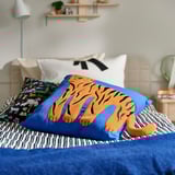Bed with blue tiger cushion, striped blanket, and colorful pillow.