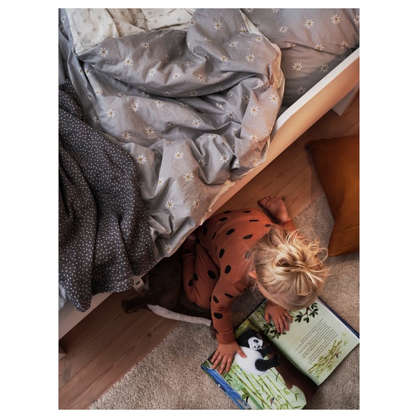 Child reading book under bed with grey and white daisy-patterned NATTSLÄNDA duvet cover.