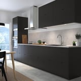 Modern kitchen with black handle-less NICKEBO cabinets, recycled materials, stainless hood & sink, plants, and chairs.