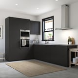 Modern black kitchen with dark cabinets, stainless steel appliances, and white countertop. Small plant and cart.