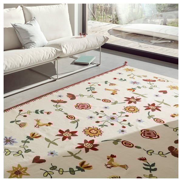 Bright living room scene with white couch, vibrant floral rug on wood floor near large window.