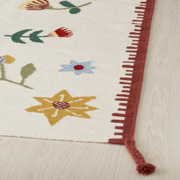 Bright, handwoven rug with floral designs and red fringe. Quality wool & cotton.