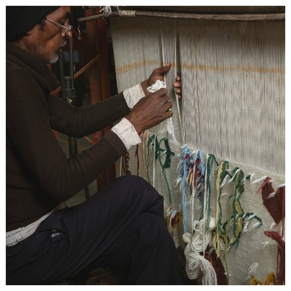 Man weaving colorful rug on loom, intricate patterns forming.