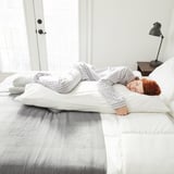 Person sleeps peacefully on soft, breathable cotton pillowcase in cozy, minimalist bedroom.