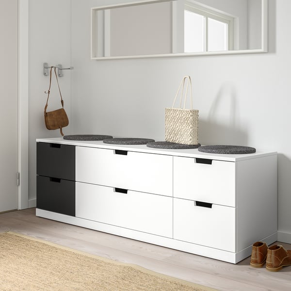 Modern white NORDLI chest with six black-handled drawers, holding a woven bag, below a mirror.