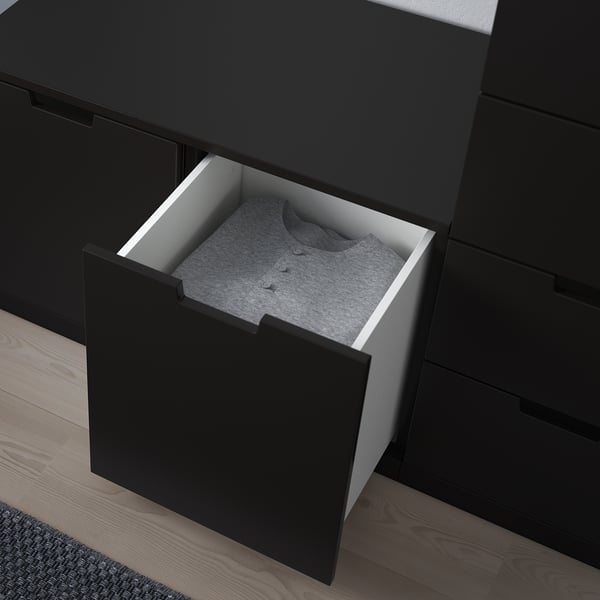 Black NORDLI dresser with one open drawer revealing folded gray sweater. Modern design, smooth drawer runners, and adjustable feet for stability.