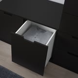 Black NORDLI dresser with one open drawer revealing folded gray sweater. Modern design, smooth drawer runners, and adjustable feet for stability.