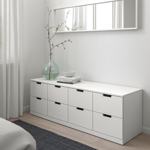 A white NORDLI chest with six drawers, books, bowl, and vase. Clean, minimalist design against a light wall.