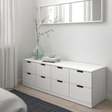 A white NORDLI chest with six drawers, books, bowl, and vase. Clean, minimalist design against a light wall.
