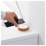 Person places smartphone on round cork wireless charger on white table.