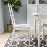 A white wooden chair with a deep seat and high back on a patterned rug, for indoor comfort.