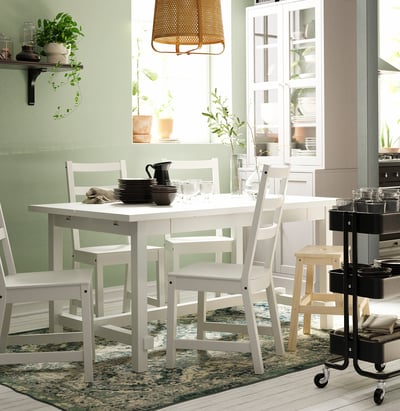 Cozy dining area with white NORDVIKEN table, chairs, rug, potted plants, and hanging lamp.
