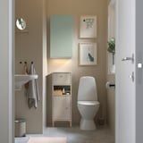 Small, beige NORSÄLVEN cabinet fits tight spaces. Compact with drawer and shelves for bathroom storage. Positioned between sink and toilet.