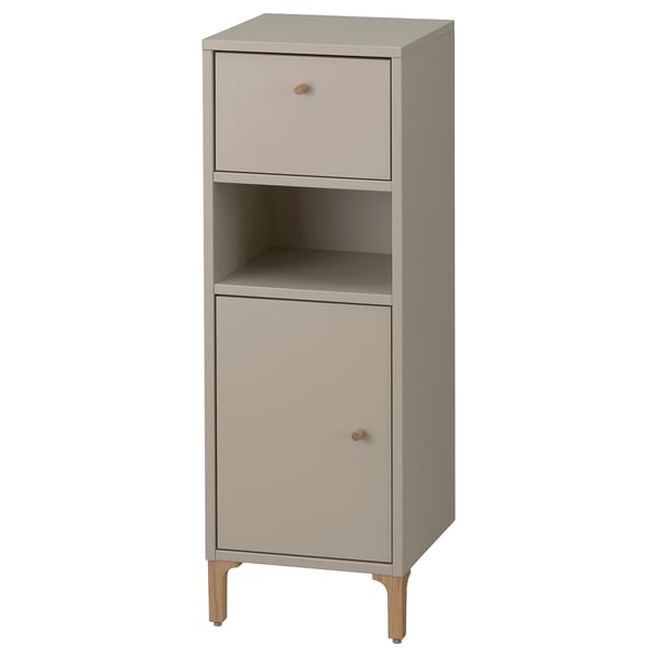 A NORSÄLVEN bathroom storage cabinet in beige. It a drawer, a door, and an open shelf. The cabinet has a slim design with wooden legs.