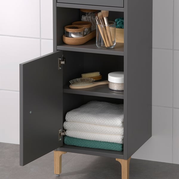 Tall grey bathroom cabinet with open and closed storage. Holds towels, toiletries, and grooming tools. Must be wall-mounted for safety.