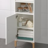 White bathroom cabinet with shelves holding towels, toiletries, and makeup tools. Efficient storage solution.