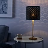 A modern lamp with a perforated shade casts intricate patterns on the wall. It sits on a round side table, illuminating a cozy living space.