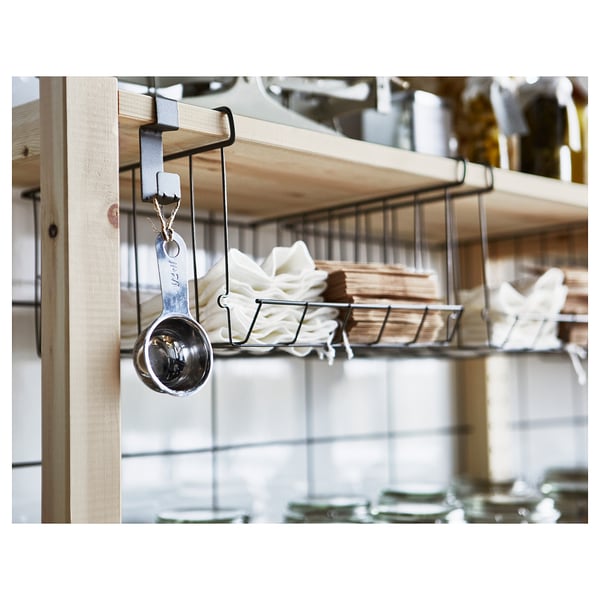 Silver measuring cup hangs on black metal hook, stored with white cloths and wooden boards on shelf.