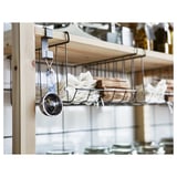 Silver measuring cup hangs on black metal hook, stored with white cloths and wooden boards on shelf.
