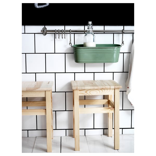 Modern kitchen scene with light wood stools against white subway-tiled wall, green metal hanging basket with glass jar.