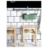 Modern kitchen scene with light wood stools against white subway-tiled wall, green metal hanging basket with glass jar.
