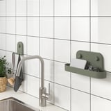 Modern kitchen wall storage solution, featuring green suction-cup holders with adjustable rack, organizing sponges and utensils beside a sleek faucet.