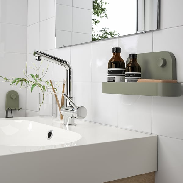 Modern bathroom with white sink, chrome faucet, and green wall organizer holding bottles.