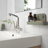 Modern bathroom with white sink, chrome faucet, and green wall organizer holding bottles.