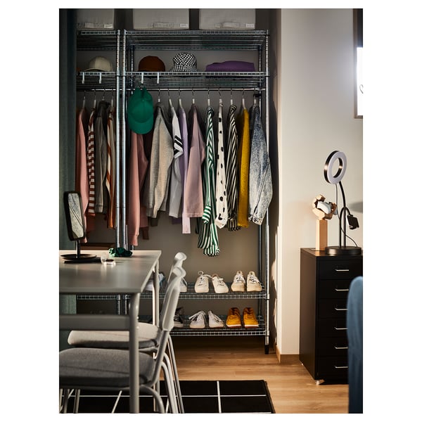 Modern wardrobe with hangers, shelves, and shoes in an organized closet. Silver metal frame, colorful clothes, and black storage drawers.