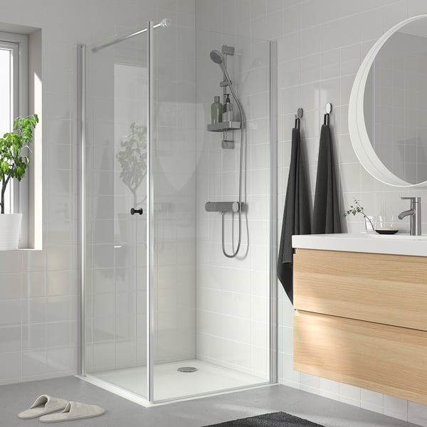 Modern bathroom with glass shower, wood counter, round mirror, dark towels, plant.
