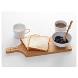 Wooden cutting board with two toast slices, bowl of jam, and two cups.