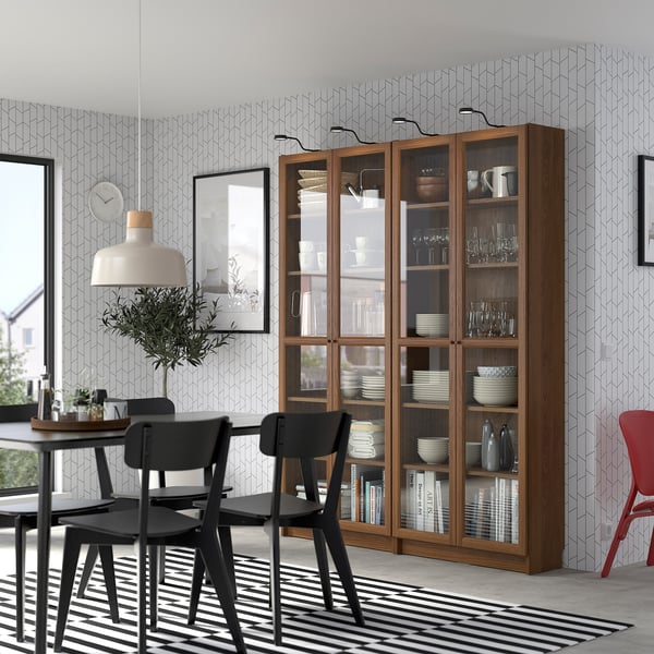 Modern dining room with OXBERG bookcase, white dishes, black chairs, striped rug, and large pendant lamp.